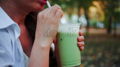 Video - Close up of woman's hand holding an iced matcha latte outdoors