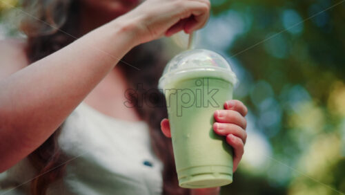 Video - Close up of woman's hand holding an iced matcha latte outdoors