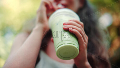 Video - Stylish young woman sipping an iced matcha outdoors, in a park