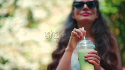 Video - Close up of a woman drinking an iced matcha in the park, in sunlight