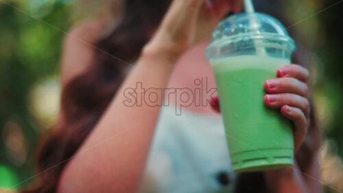 Video - Close up of a woman drinking an iced matcha in the park, in sunlight
