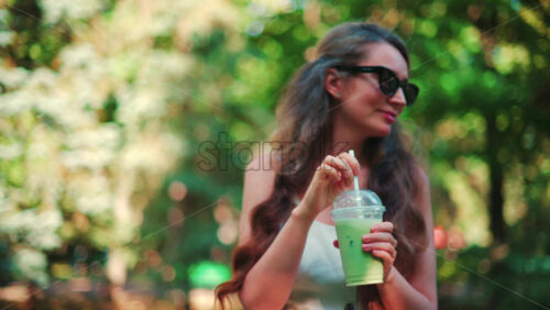 Video - Close up of woman's hand holding an iced matcha latte outdoors