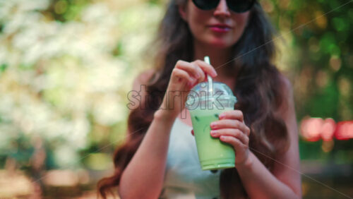 Video - Close up of woman's hand holding an iced matcha latte outdoors