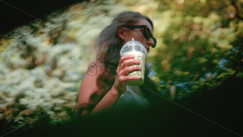 Video - Close up of a woman drinking an iced matcha in the park, in sunlight