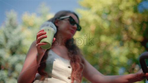 Video - Close up of woman holding an iced matcha latte outdoors while pushing a stroller