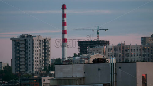 Video - City skyline with construction crane and red white chimney in soft evening light