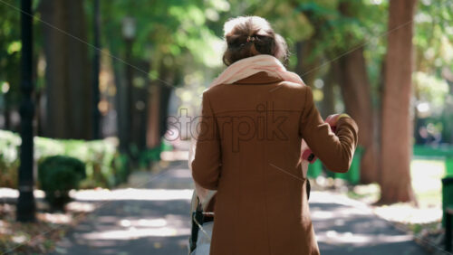 Video - A woman pushing a baby stroller along a tree lined park path on an autumn day