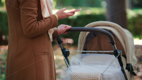 Video - A woman pushing a baby stroller along a tree lined park path on an autumn day