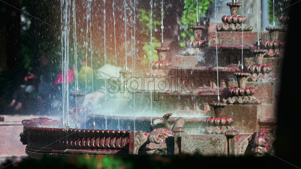 Video - View of a decorative fountain with sparkling water droplets illuminated by sunlight in a park