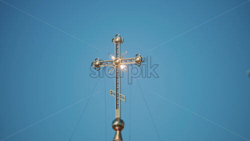 Video - Elegant metallic church cross glowing under clear blue sky