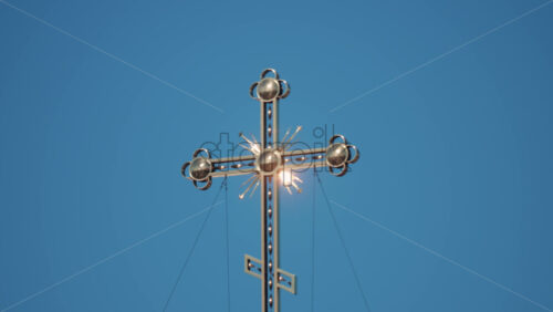 Video - Elegant metallic church cross glowing under clear blue sky