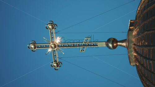 Video - Elegant metallic church cross glowing under clear blue sky. Vertical