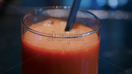 Video - Close up of a bright orange juice glass with a black straw