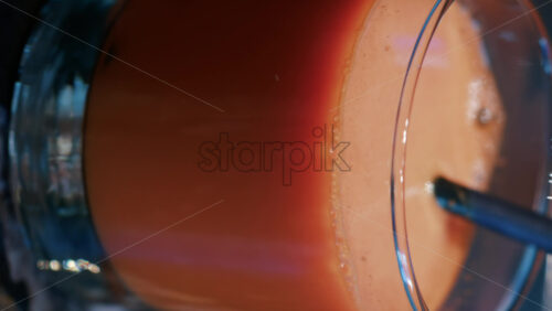 Video - Close up of a bright orange juice glass with a black straw. Vertical