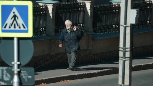 Video - Chisinau, Moldova - September 30, 2025: Senior man in warm clothing carrying a bag, walking thoughtfully along a quiet city street