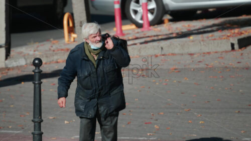 Video - Chisinau, Moldova - September 30, 2025: Senior man in warm clothing carrying a bag, walking thoughtfully along a quiet city street