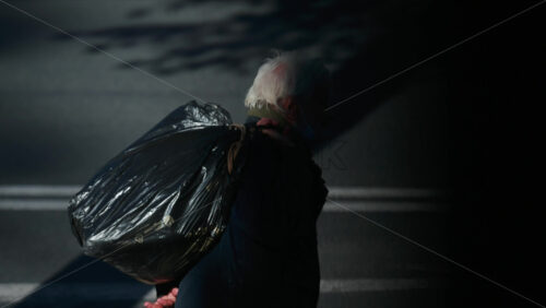 Video - Chisinau, Moldova - September 30, 2025: Senior man in warm clothing carrying a bag, walking thoughtfully along a quiet city street