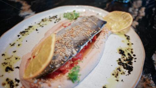 Video - Close up of a beautifully plated fish fillet with sauce, lemon slice, and herbs