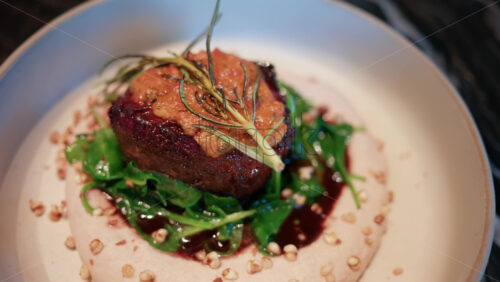 Video - Close up of a gourmet meat dish served with sauce, greens, and rosemary garnish on a white plate