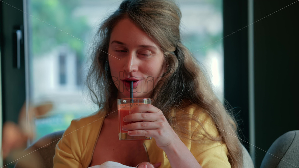 Video - Relaxed woman sipping juice through a straw while winking at the camera in a cozy cafe