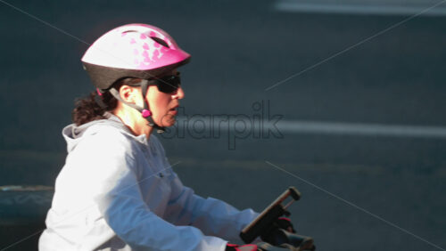 Video - Chisinau, Moldova - September 30, 2025: Active woman wearing a pink heart patterned helmet and white jacket riding an electric bike in the city