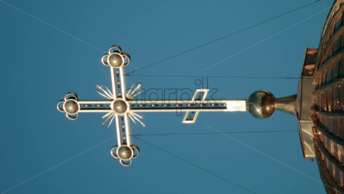 Video - Elegant metallic church cross glowing under clear blue sky. Vertical