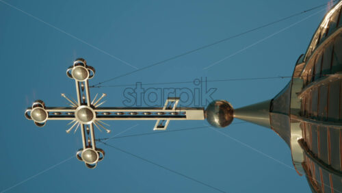 Video - Elegant metallic church cross glowing under clear blue sky. Vertical