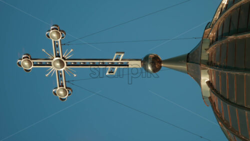 Video - Elegant metallic church cross glowing under clear blue sky. Vertical