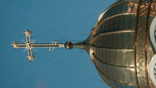 Video - Elegant metallic church cross glowing under clear blue sky. Vertical