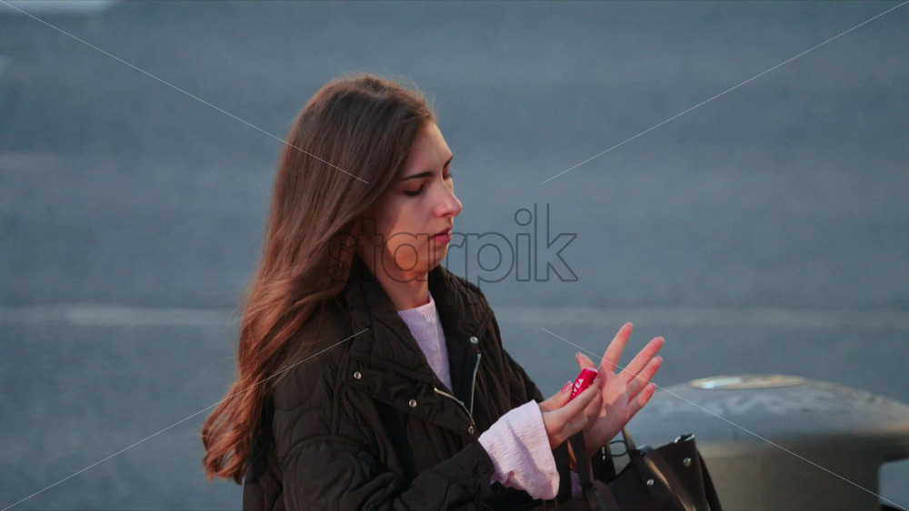 Video - Chisinau, Moldova - September 30, 2025: Young woman walking along a crosswalk, holding a black handbag and wearing a dark quilted jacket