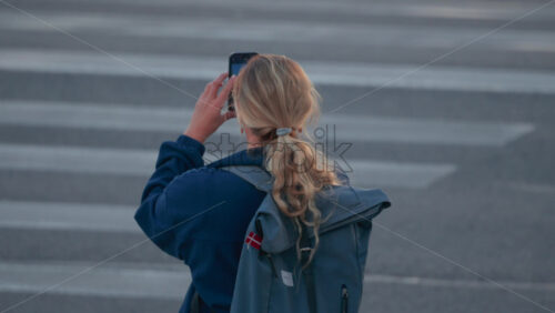 Video - Blonde woman with a ponytail and blue backpack photographing the city using her smartphone