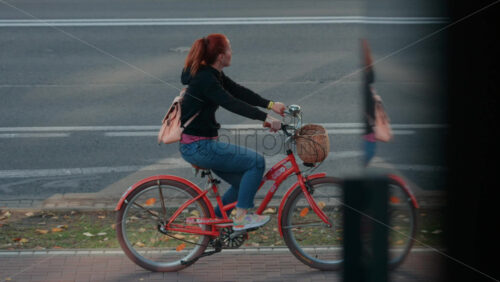 Video - Chisinau, Moldova - September 30, 2025: Red haired woman riding a bicycle with a front basket along a busy street lined with trees