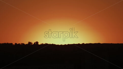 Video - A peaceful view of an orange yellow sky above dark silhouetted hills during sunset