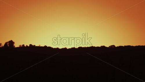 Video - A peaceful view of an orange yellow sky above dark silhouetted hills during sunset