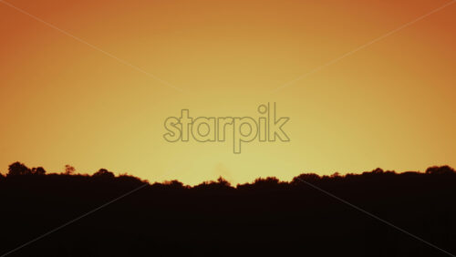 Video - A peaceful view of an orange yellow sky above dark silhouetted hills during sunset