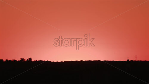 Video - Stunning sunset with the sun descending behind the hills and a bird flying across the orange sky