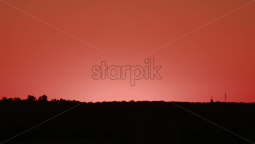 Video - Stunning sunset with the sun descending behind the hills and a bird flying across the orange sky