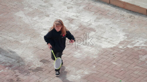 Video - Chisinau, Moldova - September 30, 2025: A cheerful young girl plays badminton outside on a paved courtyard, full of joy and energy