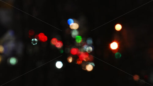 Video - Timelapse of out of focus colorful traffic lights shimmering down a dimly lit street, creating a vibrant atmosphere in a calm neighborhood. The surrounding trees frame the mystical scene at night.