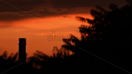 Video - An industrial chimney stands against a colorful sunset. The sky transitions from orange to dark hues.