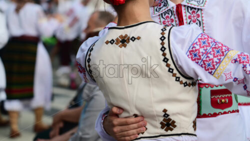 Video - Dancers in vibrant traditional outfits perform lively folk dances at a summer festival in a community square, celebrating local customs and culture with joyful expressions. Slow motion