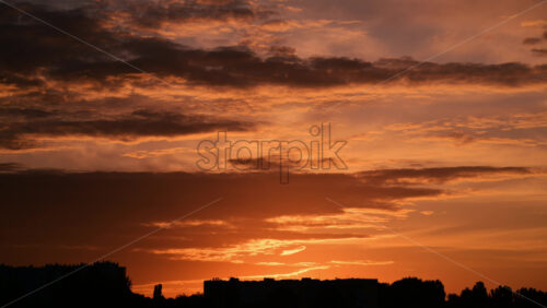Video - A stunning sunset paints the sky with shades of orange, pink, and purple. The clouds reflect the warm light, creating a peaceful and tranquil view in the evening. City silhouette and lake