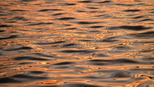 Video - Golden sunlight dances on the calm water's surface, creating beautiful reflections at dusk. Reflection of sunset on water waves