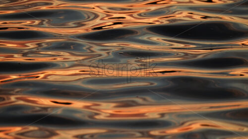 Video - Golden sunlight dances on the calm water's surface, creating beautiful reflections at dusk. Slow motion reflection of sunset on water waves