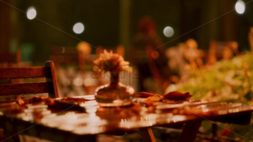 Video - Rain gently falls in a peaceful park, creating a serene atmosphere. A lone person sits on a wooden chair, surrounded by wet foliage and dim lights in the evening.