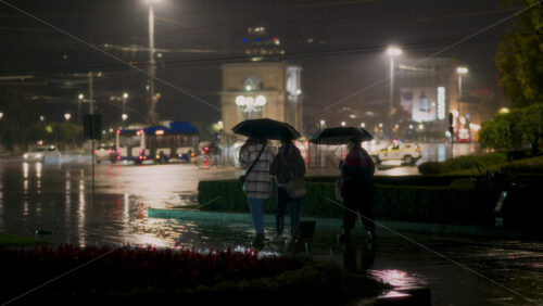 Video - People navigate near city center at night under umbrellas as rain pours down. Triumphal Arch on background. Chisinau, Moldova