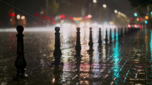 Video - Rain falls steadily on city streets, creating mirrored reflections on the pavement. Streetlights and vehicle headlights illuminate the scene, adding vibrant colors to the rainy atmosphere.