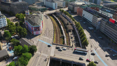 Video - Copenhagen, Denmark - August 6, 2025: Aerial drone view of a bustling intersection showing cars, buses, cyclists, and red S-train passing through the city center