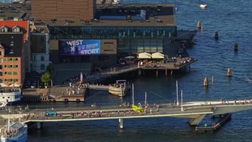 Video - Copenhagen, Denmark - August 6, 2025: Aerial drone view of the Royal Danish Playhouse on Copenhagen's waterfront, with people walking and cycling across Inderhavnsbroen bridge