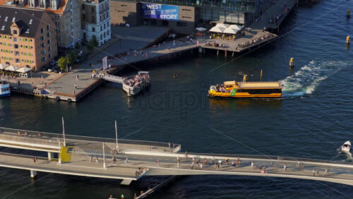 Video - Copenhagen, Denmark - August 6, 2025: Aerial drone view of boats and a canal tour passing under Inderhavnsbroen pedestrian and bicycle bridge